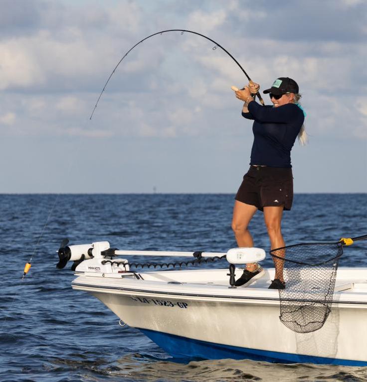 A woman reels in a fish as her fishing pole bends dramatically under the pressure.