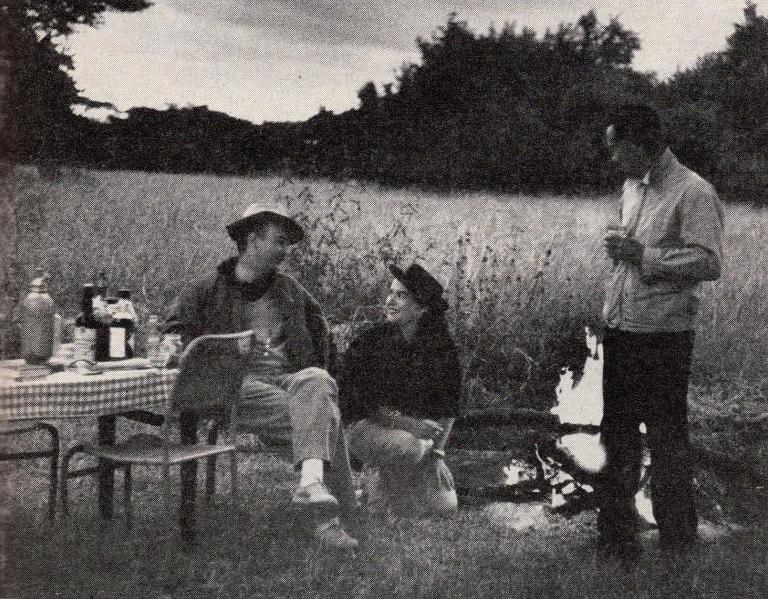 Robert Grimm, Virginia Kraft, and guide gather around a campfire, holding martinis, on the African plains.