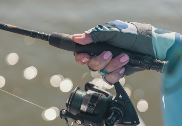 A woman&rsquo;s manicured hand holds a fishing pole at it&rsquo;s reel.