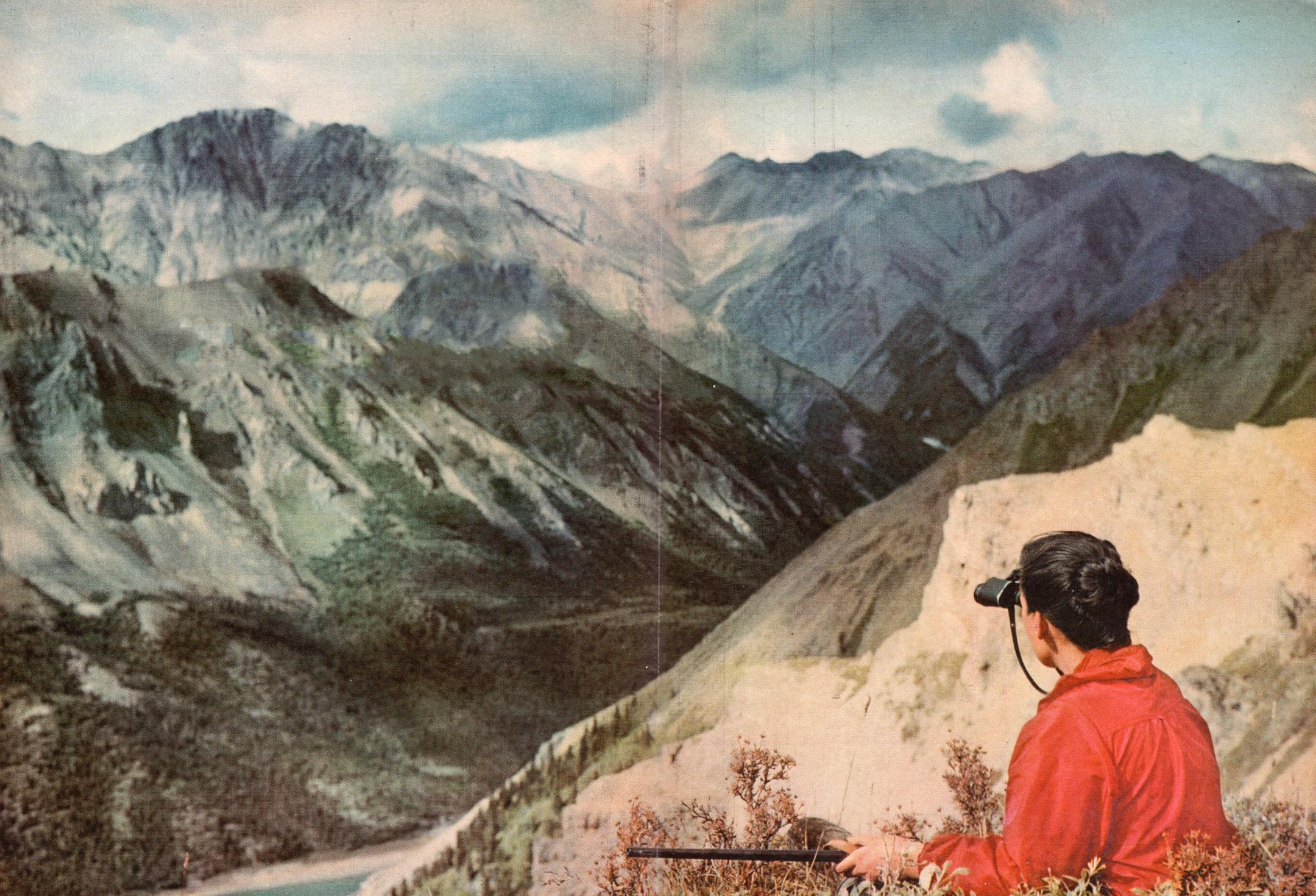 woman with red coat and binoculars looking at a beautiful mountain scenery in the distance